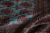 A fine Bokhara carpet folded to show its soft, lustrous wool pile and intricate geometric border.