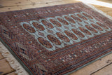 Angled view of a vintage Bokhara rug highlighting its plush pile and repeating rust-colored guls.