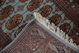 Folded corner of a fine Bokhara rug revealing its plush pile, intricate border, and clean selvage.