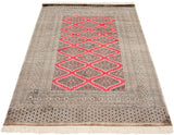 Angled perspective of a vintage Pakistani Turkmen rug highlighting its repeating red diamond medallions.