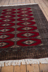 Angled view of a vintage Turkmen design rug showing repeating red gul medallions and ivory fringe.