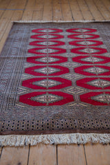 Long perspective view of a vintage Turkmen rug with its cherry red gul pattern and ivory fringe.