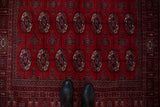 A perspective view of the plush wool pile and geometric border of a cherry red Bokhara rug.