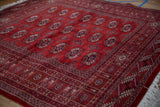 Angled view across the plush, cherry red pile of a fine Bokhara rug with repeating gul medallions.
