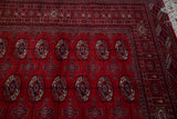 Corner of a cherry red vintage Bokhara rug showing the intricate geometric border and ivory fringe.