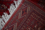 Corner of a red Bokhara rug showing the tight hand-knotted reverse and ivory fringe.