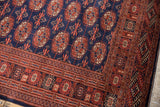 Detailed corner of a vintage Bokhara rug with repeating gul medallions and an intricate geometric border.