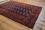 Fine vintage Bokhara rug from an angle, showcasing the sheen on its tightly woven navy and rust pile.