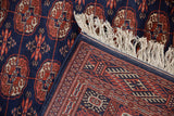 Close-up of a vintage Bokhara rug's corner showing the plush pile, detailed border, and ivory fringe.