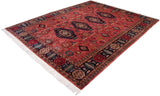 Geometric navy border with pomegranate motifs on dusty raspberry field, vintage Pakistani rug corner.