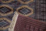 Folded corner of a Pakistani rug revealing a mauve back, original side cord, and hand-knotted ivory fringe.