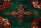 Detailed gul medallion in rust and navy blue on the plush emerald green wool pile of a vintage Bokhara carpet.