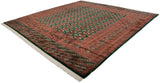 Angled view of a vintage Bokhara square carpet with lustrous emerald green and rust gul medallions.