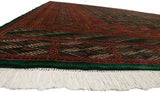 Low-angle view of a vintage Bokhara carpet's plush pile, emerald green border, and clean ivory fringe.