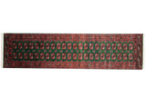 Vintage Bokhara rug runner with repeating gul medallions in rust and navy on a deep emerald green field.