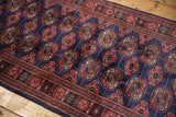 A close-up view of the fine Bokhara rug's repeating rust gul medallions on a plush navy pile.