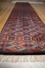 Low perspective along a vintage Bokhara runner, highlighting the repeating gul medallions and ivory fringe.