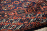 Angled view of a Bokhara rug's plush navy pile, intricate rust border, and ivory fringe.