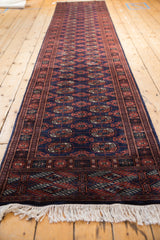 Angled view of the entire vintage Bokhara runner, highlighting its repeating navy and rust gul pattern.