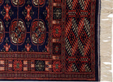 Corner of a vintage Bokhara runner showing the geometric border, plush navy pile, and ivory fringe.