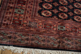 Plush wool corner of a vintage Bokhara carpet with detailed geometric borders in black and terracotta.