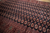 Angled view of a vintage Bokhara carpet's plush, lustrous pile and repeating gul medallions.