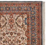 Corner view of a Sultanabad rug with palmette borders, a denim blue edge, and ivory fringe.