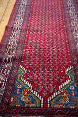 Angled view of a vintage Persian runner, detailing the boteh-filled red field and wave border.