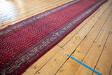 Long perspective view of the vintage Tajabad runner's intricate red boteh pattern and wave border.