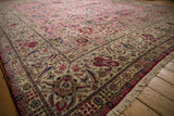Low angle across a pink vintage Tabriz carpet, detailing its intricate ivory floral border and fringe.