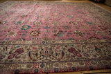Angled view of a vintage Tabriz carpet's pink floral field and intricate silver border.