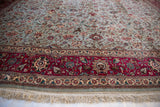 Corner view of a vintage Tabriz carpet showing the raspberry red pictorial border and hand-knotted fringe.