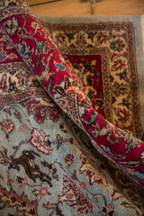 Rolled vintage Tabriz rug showing plush pile, red border, and blue field with prancing deer.