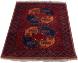 Angled view of a vintage Ersari design rug with geometric guls against a dark brick red background.