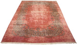 Angled view of a vintage Kerman rug's dusty rose field and oversized scrolling vine border.