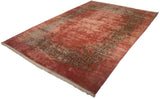 Angled perspective on a vintage Kerman carpet showing its open dusty rose field and scrolling border.