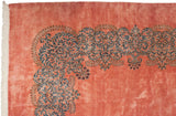 Scrolling blue Rococo-style vine border and white fringe on a dusty rose vintage Kerman carpet.