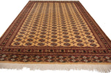 Angled perspective down the length of a vintage Bokhara carpet with repeating geometric guls on a gold field.