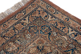 Corner detail of an antique Kermanshah carpet with its navy blue cartouche border and ivory fringe.