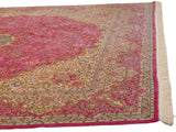 Corner of a vintage Kerman carpet showing a plush pink field and detailed ivory floral border.