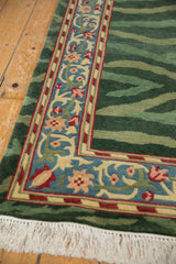 Corner detail showing the scrolling floral border, striated green pile, and white fringe.