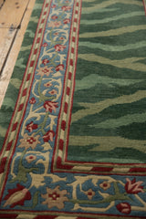 A scrolling palmette border in blue and red runs alongside the striated green field of a vintage rug.