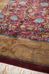 Detail of vintage Indian Arts and Crafts carpet: wine red field, blue florals, gold leaves, white fringe.