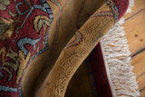 Rolled Indian Arts and Crafts rug showing plush wine red, gold, and blue floral scroll patterns.