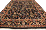 Angled view of the vintage Indian carpet's scrolling vinery and terracotta border on a navy field.