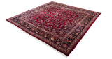 Angled view of a square vintage Sarouk carpet showing its ruby red field and elaborate floral border.