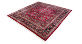 Angled view of a vintage Sarouk square carpet with a ruby red floral field and navy border.