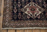 Corner of a vintage Ardebil rug showing the floral border, navy field, and intact side cord selvage.