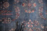 Black boots on vintage Laristan carpet, dusty denim blue, cherry red floral sprays.