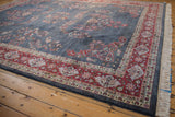 Vintage Laristan rug's dusty denim field, red floral border, and ivory fringe at the corner.